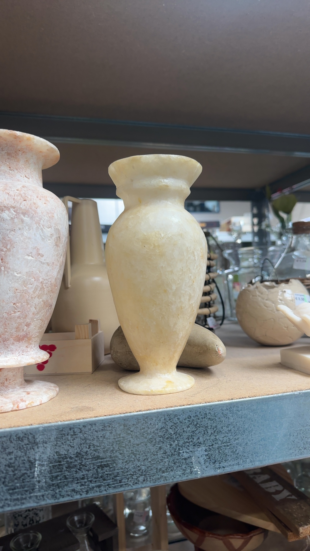 Alabaster urn-shaped vase with pedestal base and flared rim, featuring natural stone veining, on a shelf.
