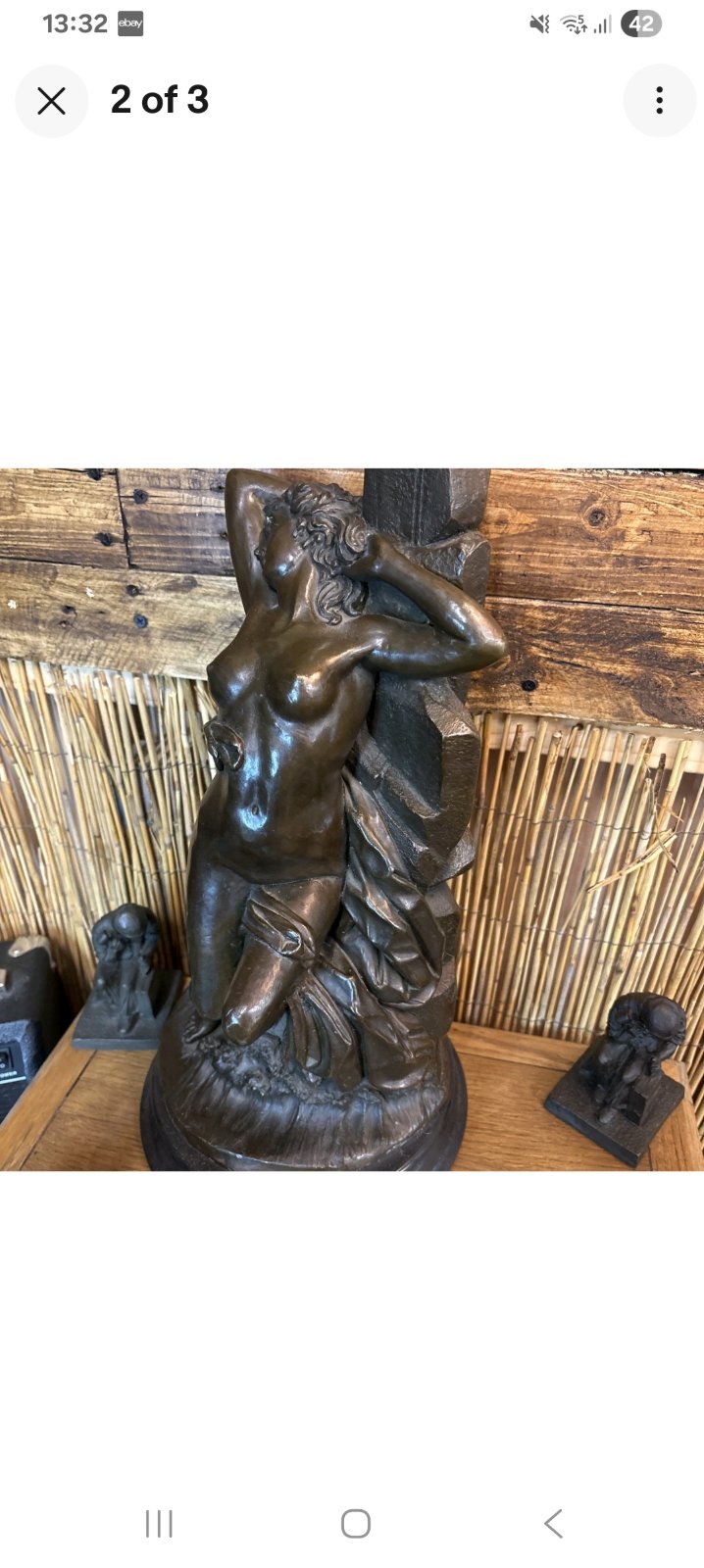 Glossy cast sculpture of a draped nude female figure leaning against a rocky column with hands behind her head, surrounded by stylized waves. - view 1