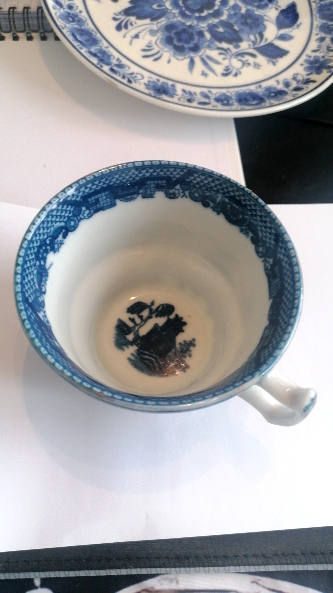 Blue and white porcelain teacup with traditional Willow Pattern design, featuring pagodas, bridges, and willow trees. - view 1