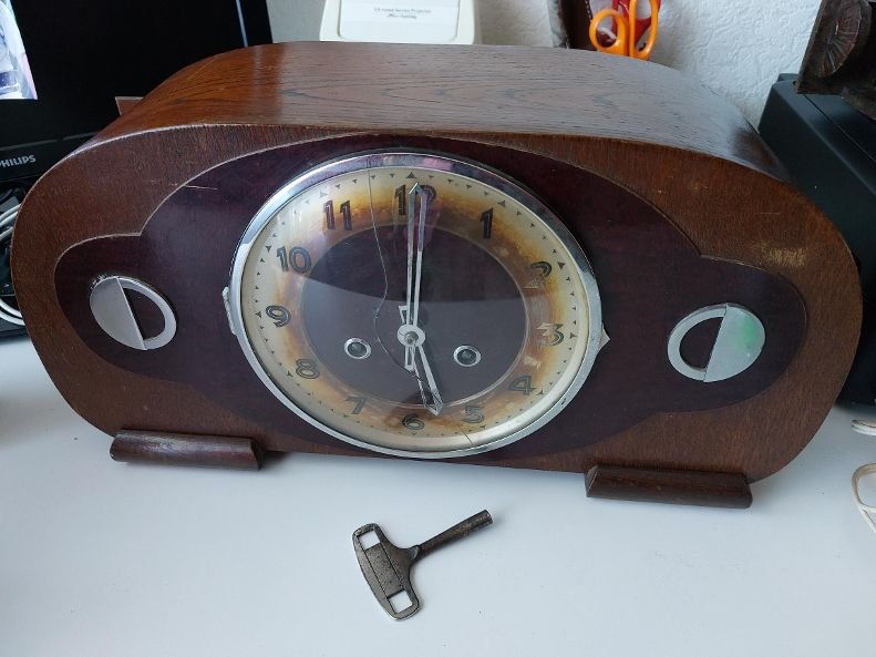 Art Deco wood mantel clock with a curved top, cracked glass face, and a metal winding key resting in front of it.