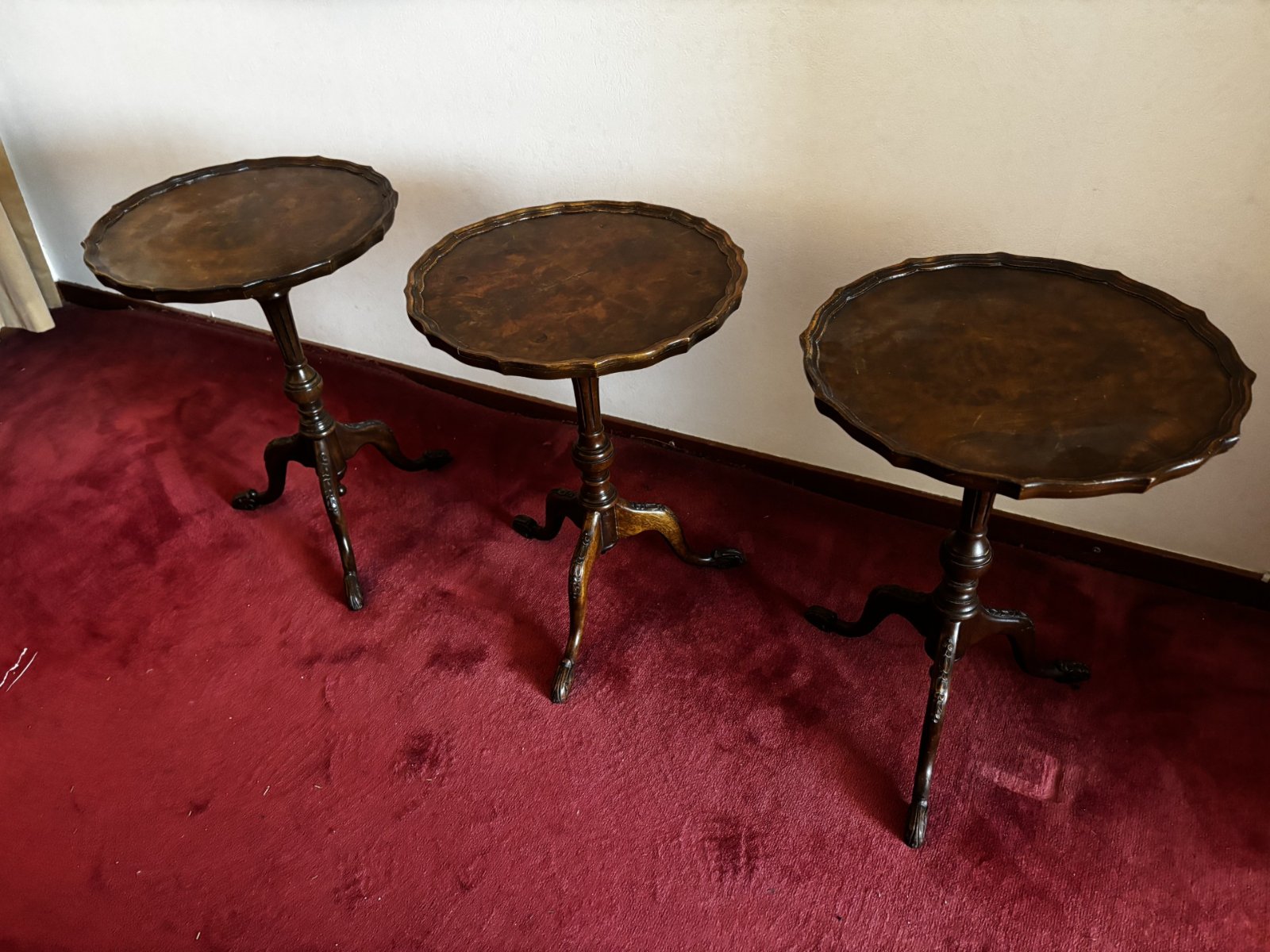 Three matching mahogany tripod wine tables with scalloped pie-crust edges on a red carpet.