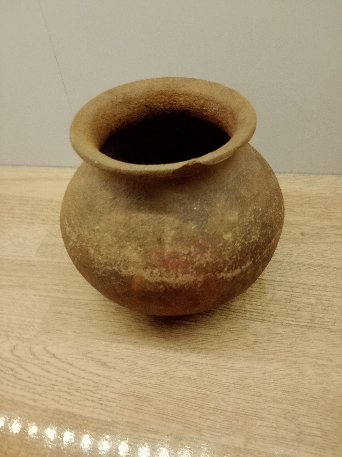 Small unglazed earthenware pot with rounded body and flaring rim, showing earthy tones of brown and grey. - view 1