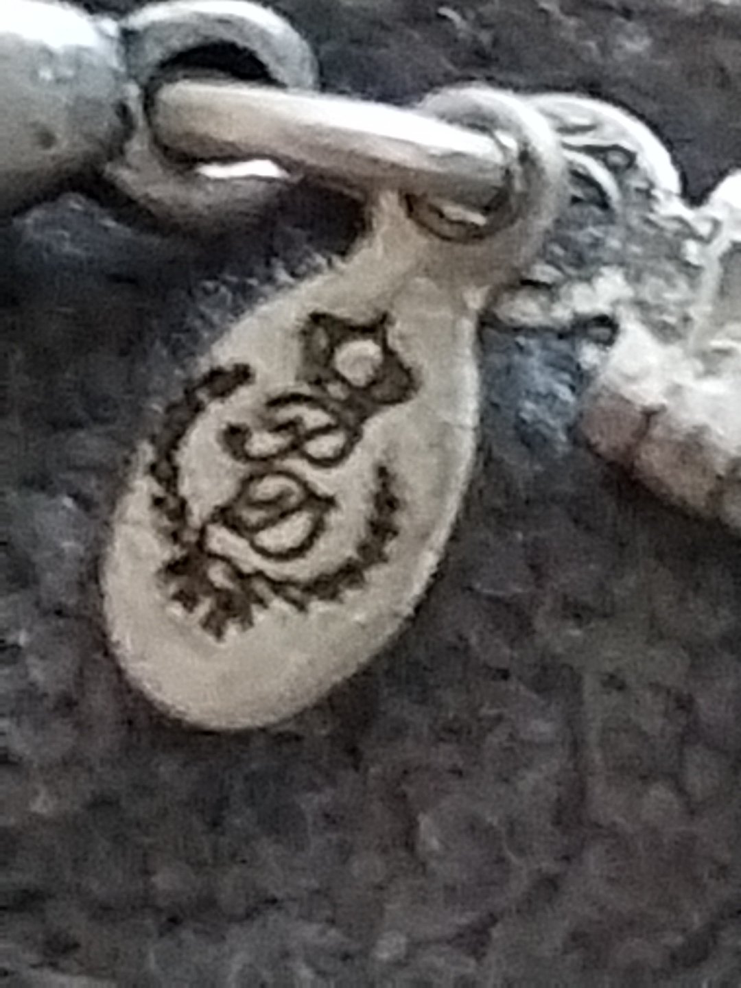 Close-up of a silver-tone oval hang tag with the 1928 Jewelry Company logo featuring three loops, a crown, and a laurel wreath.