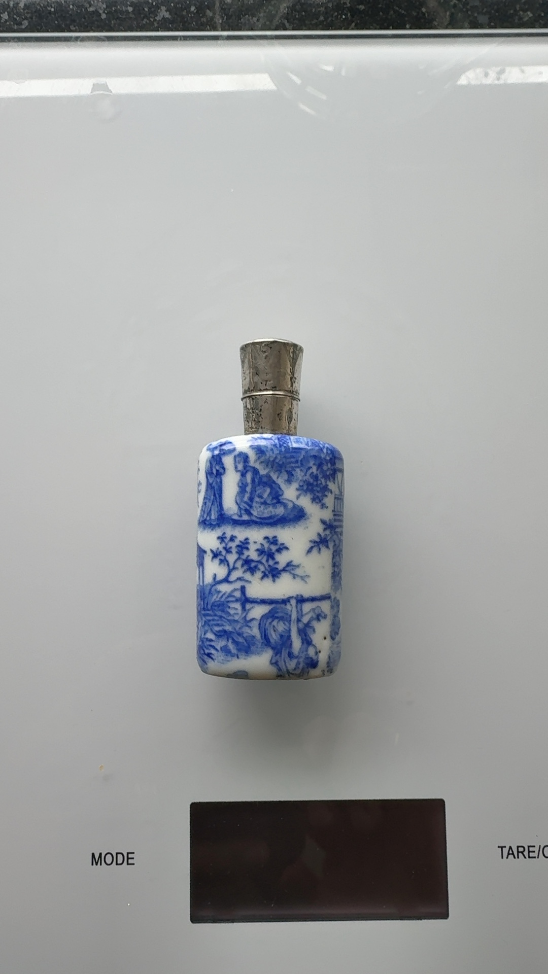 Small blue and white ceramic scent bottle with oriental-style decoration and a hinged silver cap, held in a hand for scale. - view 1