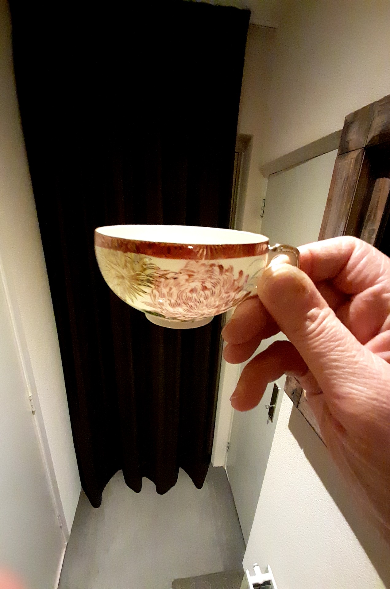 A translucent Japanese porcelain teacup held to light, revealing a geisha lithophane portrait in the base. - view 1