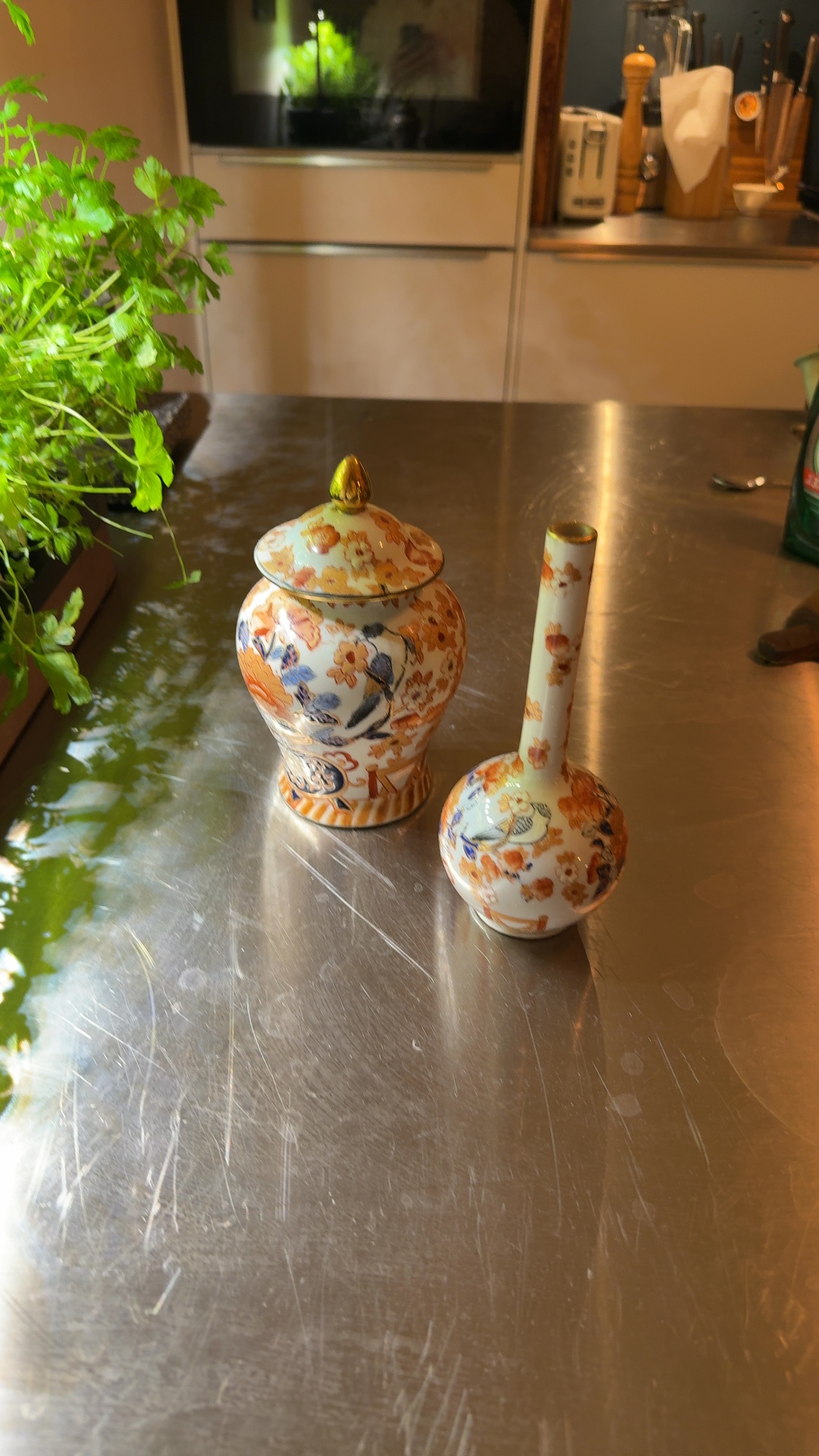 Pair of Japanese Imari-style porcelain decorative pieces, including a lidded ginger jar and a tall bottle vase, adorned with floral and bird motifs in orange, blue, and gold.