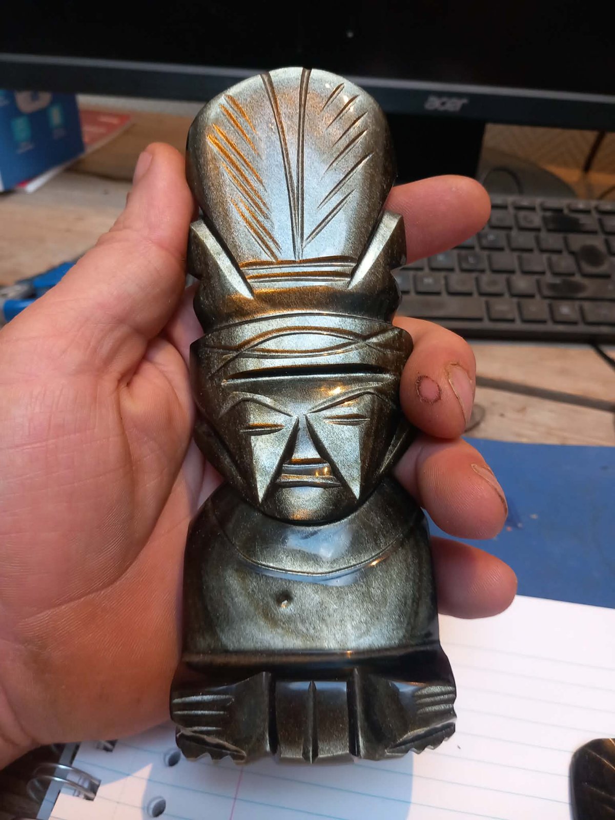 Hand holding a modern Mexican carved figure made of gold sheen obsidian with sharply incised Mesoamerican features. - view 1