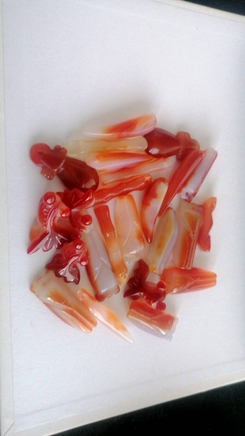 Pile of carved carnelian and agate gemstone cabochons and pendant blanks in red, orange, and white hues.