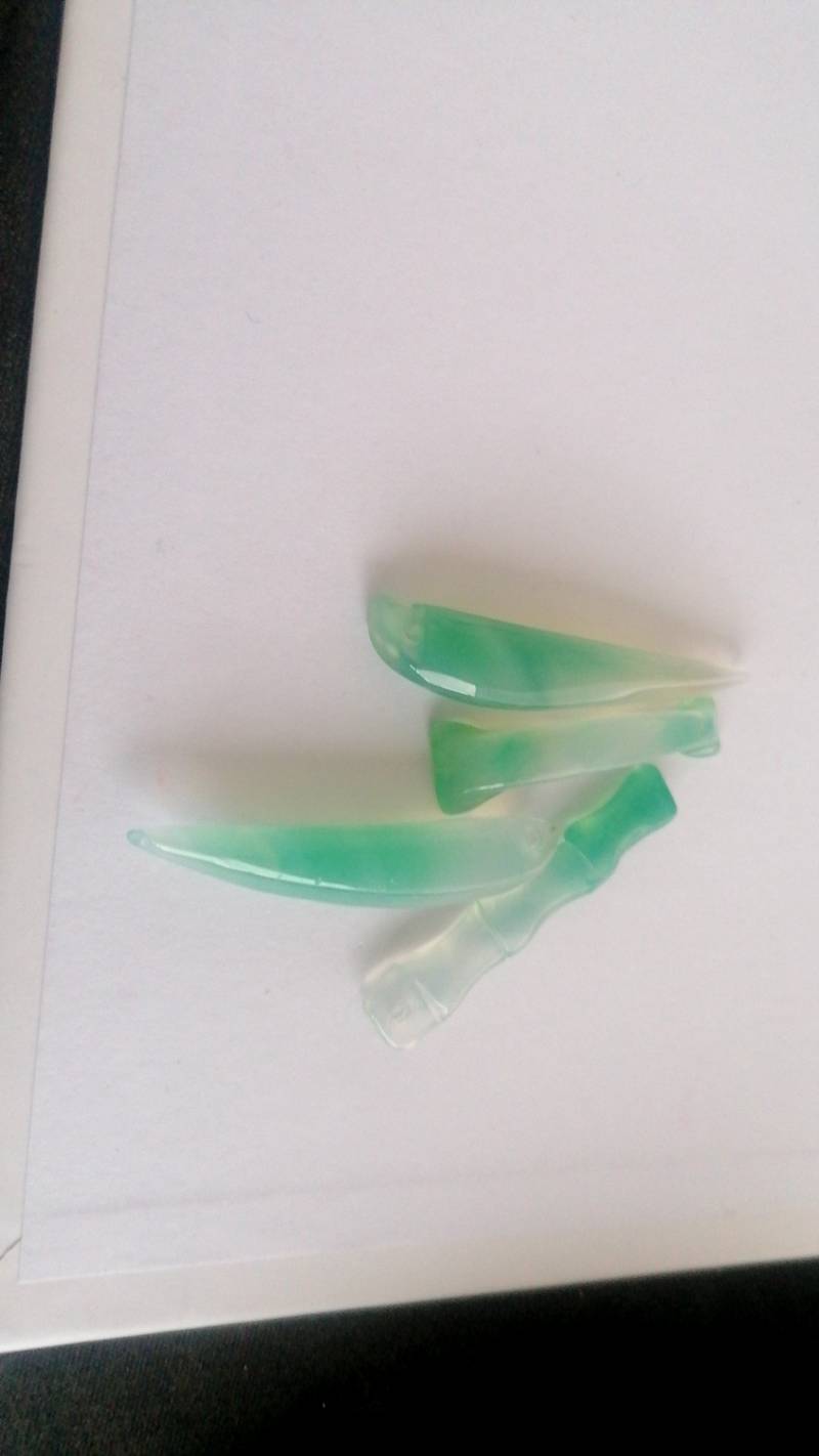 Four small, polished, translucent green and white carved chalcedony or jadeite pieces on a white background, resembling small tools or ornaments.