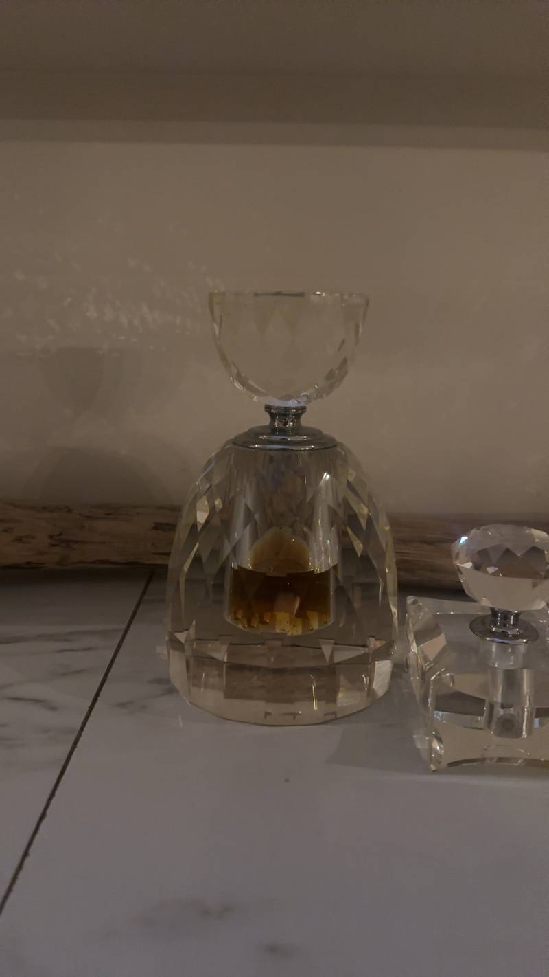 A heavy faceted Baccarat crystal perfume bottle with a large stopper, featuring deep geometric cuts and a silver collar on a marble surface.