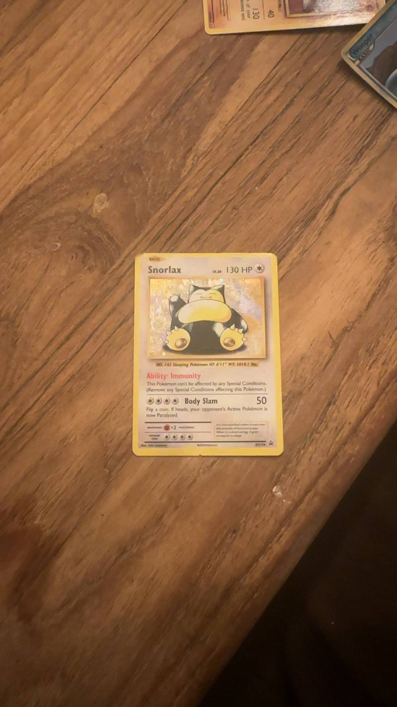 A Snorlax XY179 Black Star Promo Pokemon card with holographic art sitting on a wooden surface.