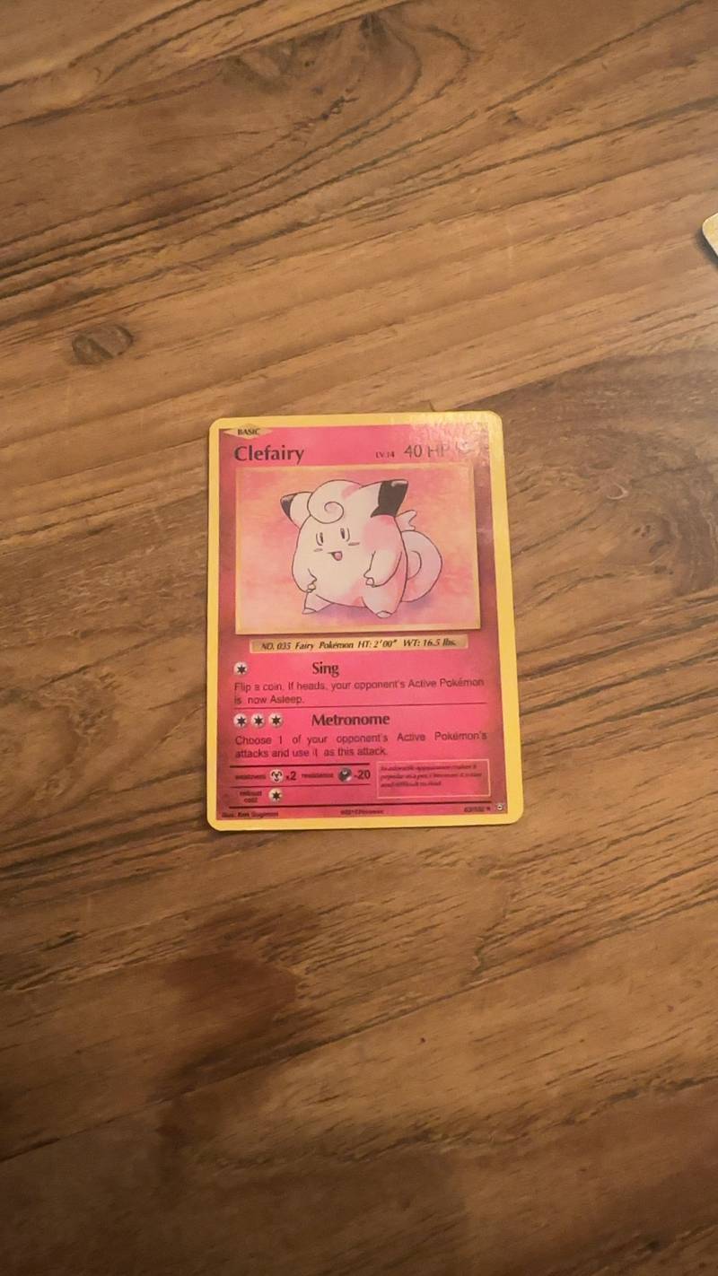 Pokemon TCG Clefairy Base Set card, showing the pink fairy creature and card details against a wood background.