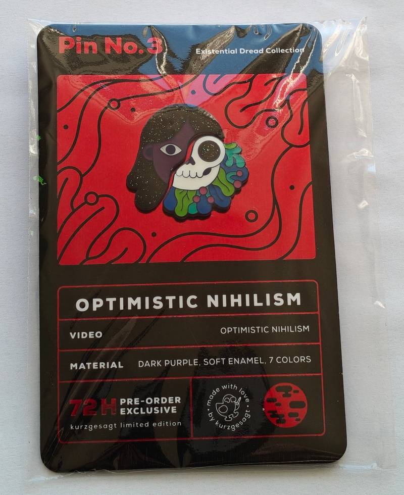 Kurzgesagt Optimistic Nihilism enamel pin mounted on a red and black backing card inside a clear plastic protective bag.