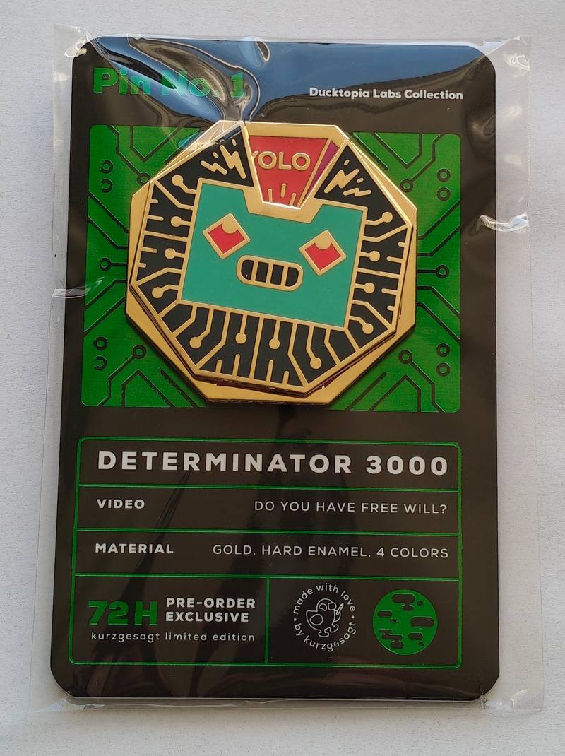 A Kurzgesagt Determinator 3000 hard enamel pin on its original green and black 'Ducktopia Labs' backing card, sealed in plastic.