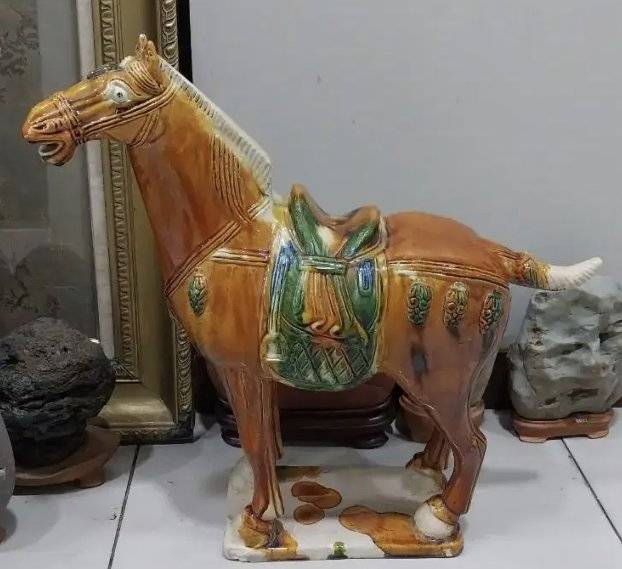 A ceramic horse figure with amber and green sancai glaze standing on a white base, inspired by Chinese Tang Dynasty tomb pottery.