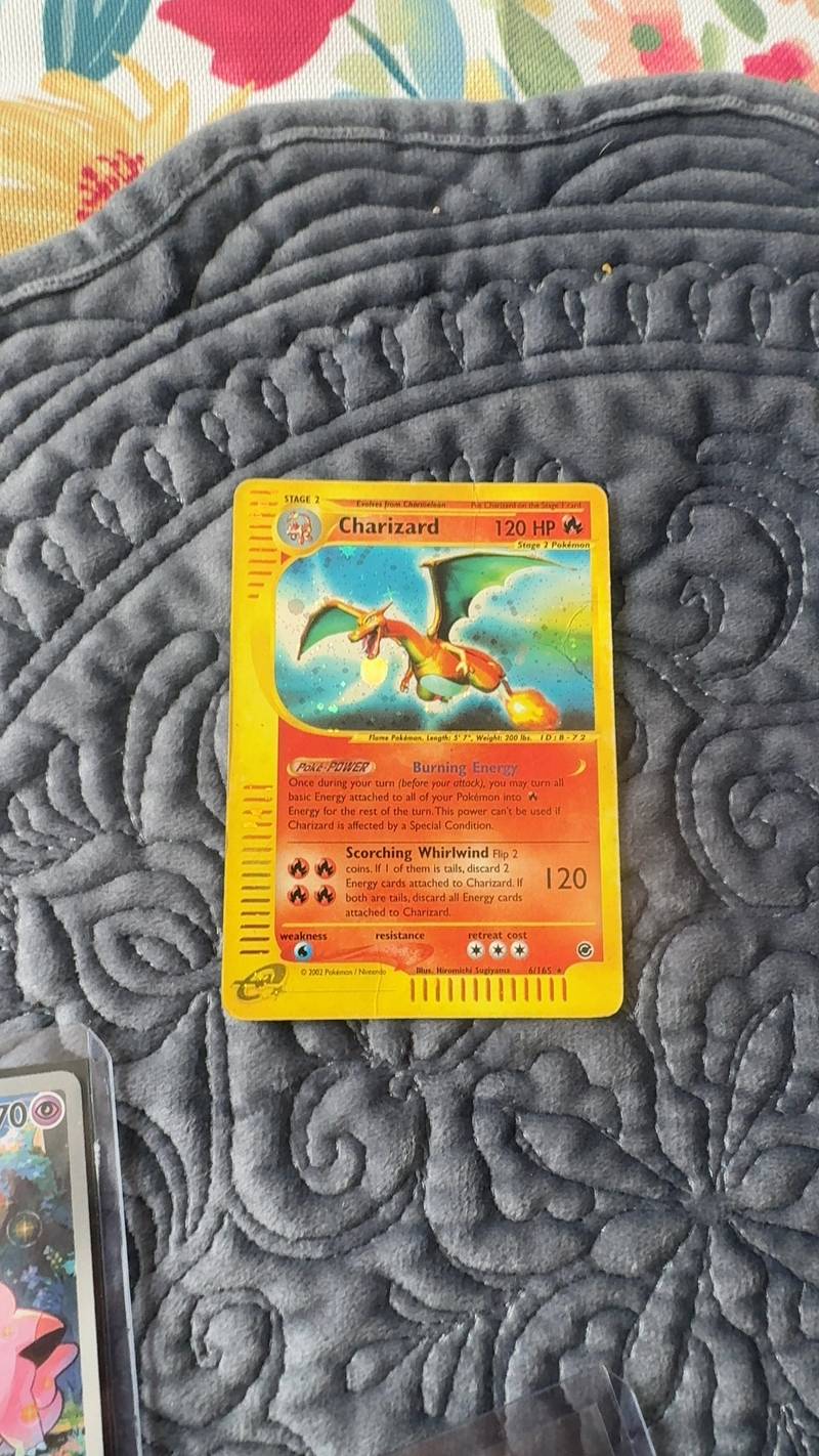 A 2002 Pokémon Expedition Charizard Holofoil card with a visible vertical crease and edge wear on a grey textured surface. - view 1