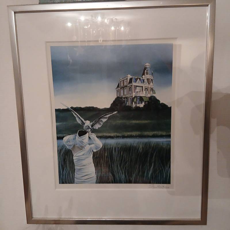 Framed surrealist art print by Ann Martino featuring a bandaged figure, a flying gull, and an old mansion on a hill. - view 1