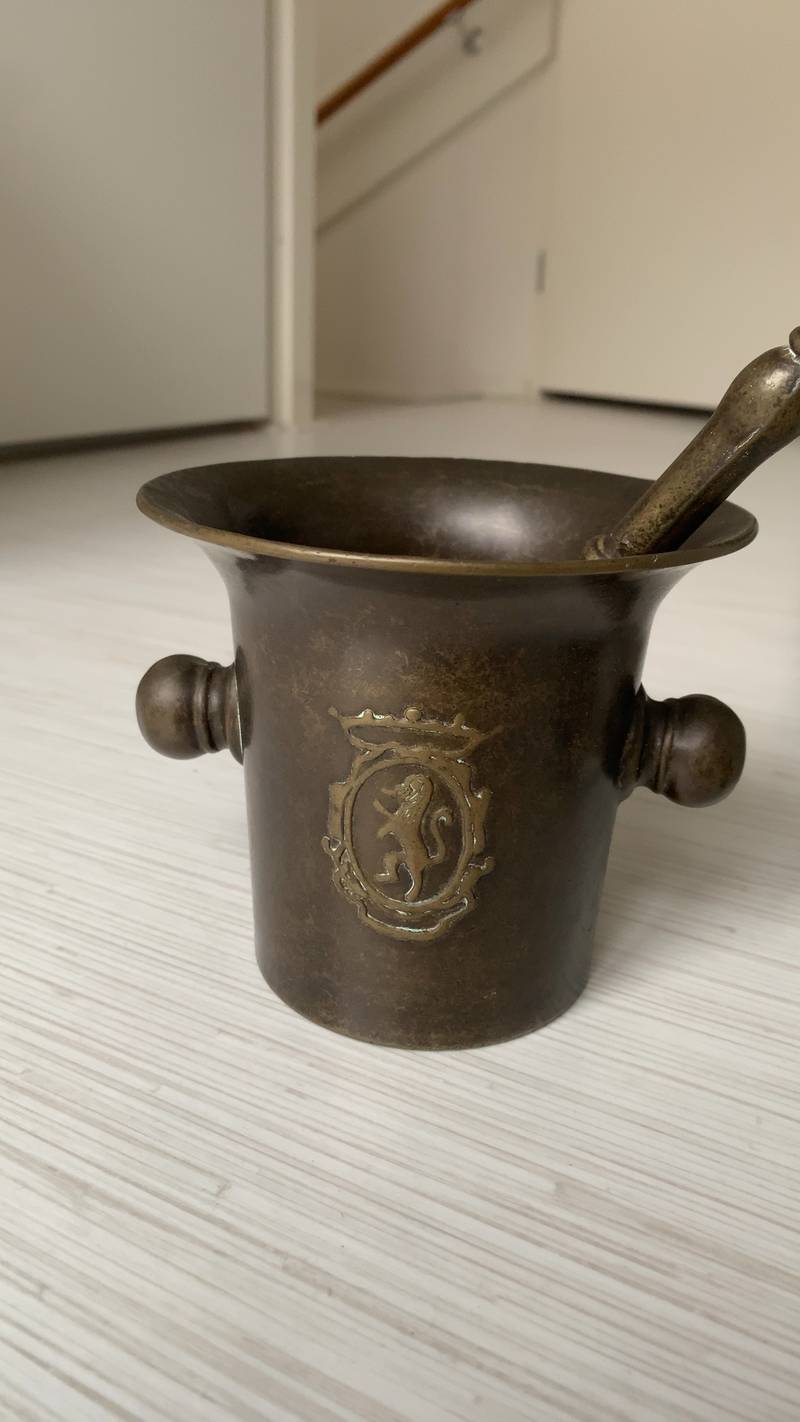 Antique bronze mortar and pestle with a lion rampant armorial crest, showing aged patina.
