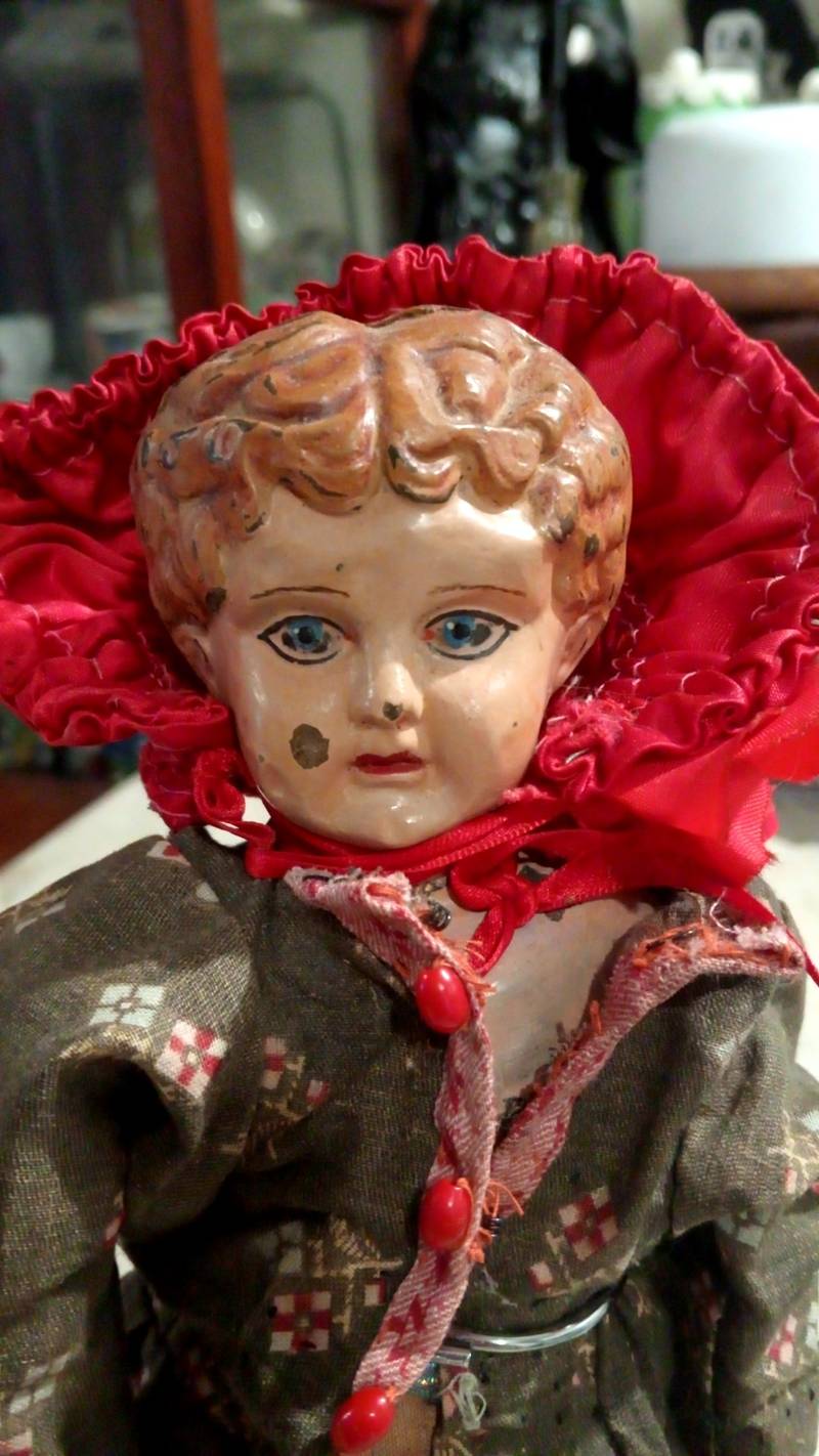 Vintage mid-19th century papier-mâché doll with a red bonnet and brown print dress, showing a 'PATENT' stamp on the shoulder. - view 1