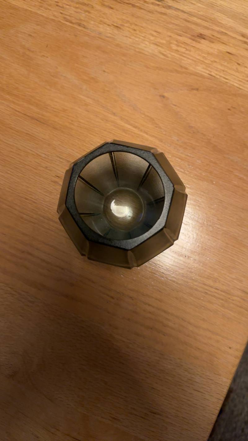 A smokey gray faceted glass tealight holder with a frosted exterior and polished rim sitting on a wooden table. - view 1