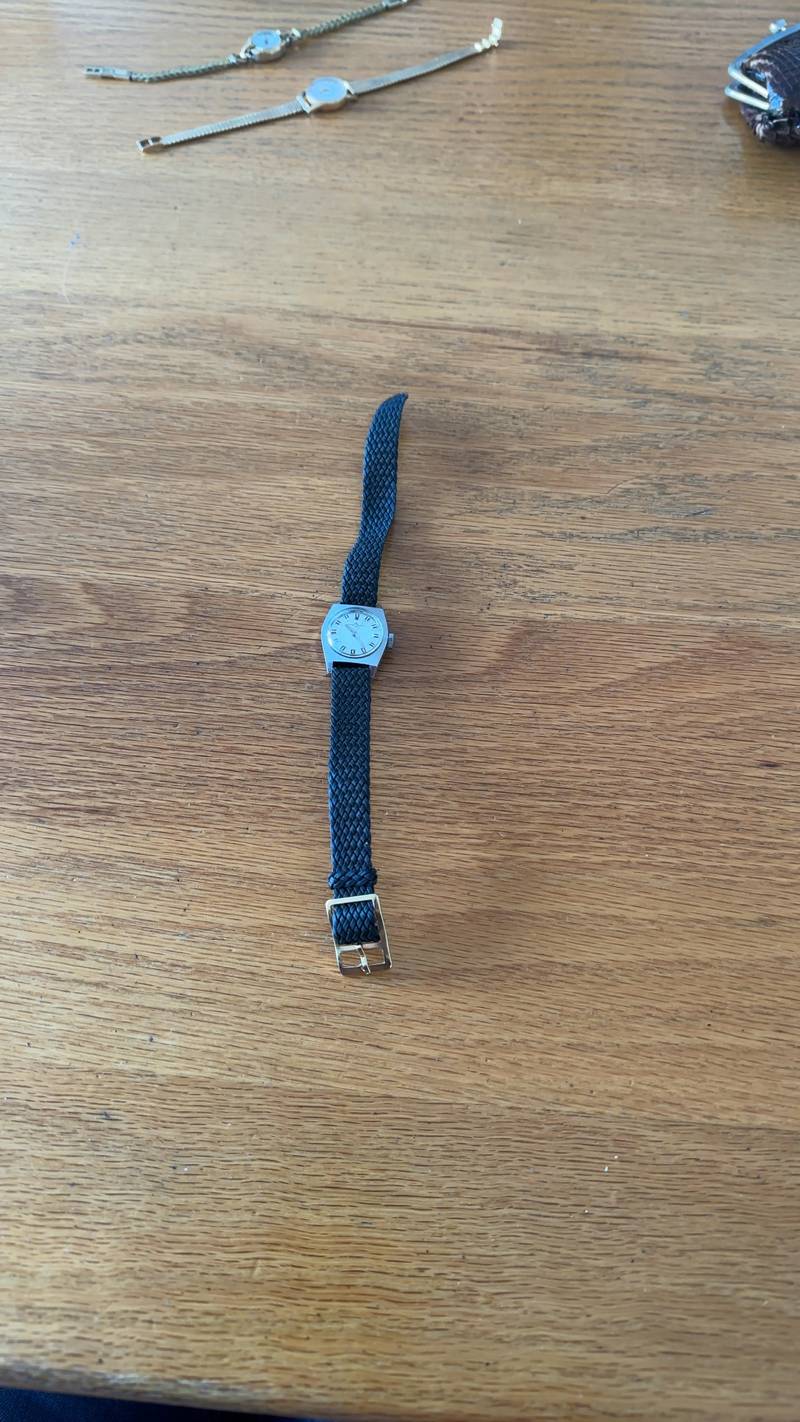 Vintage Baume & Mercier ladies watch with a tonneau-shaped steel case and black braided strap on a wooden surface. - view 1