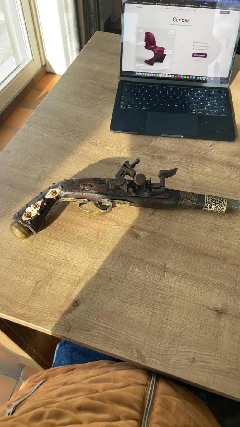 Side profile of an antique-style flintlock pistol reproduction with ornate barrel and inlaid grip on a wooden table. - view 1