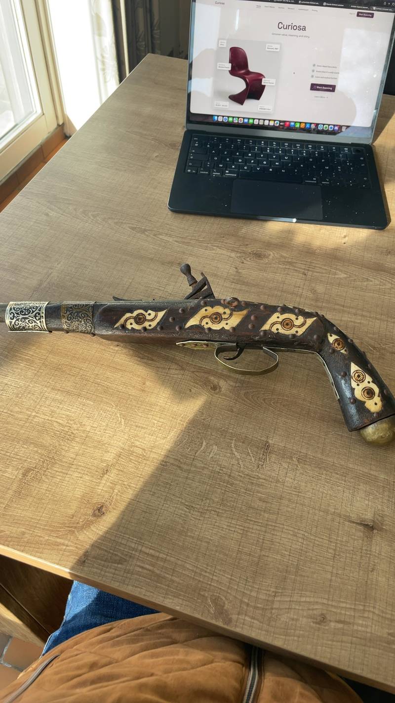 Ottoman-style decorative flintlock pistol with intricate bone or ivory inlays and brass tacks on a wooden table next to a laptop. - view 1