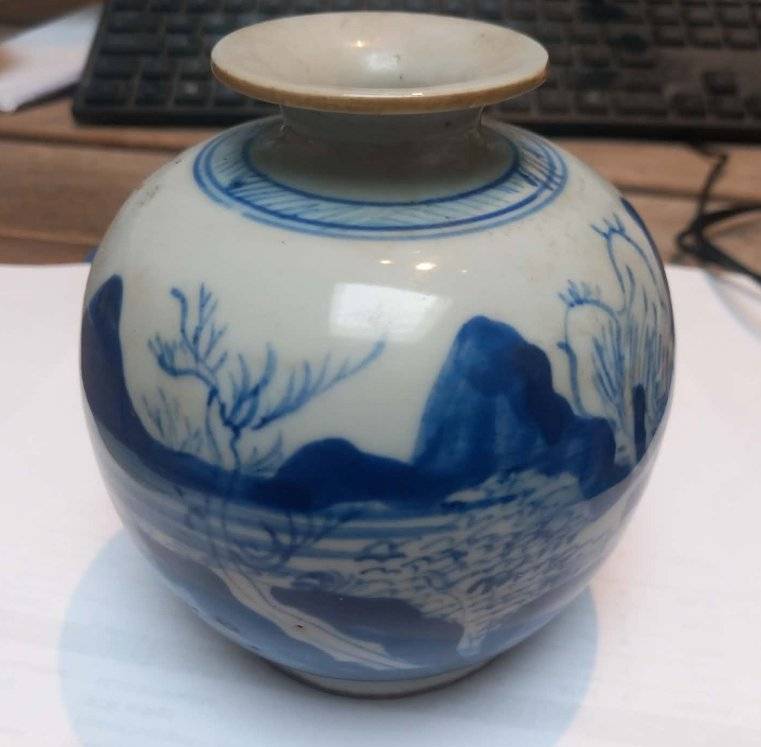 A small globular Chinese blue and white porcelain jar with a landscape scene and a wide, flat rim, shown on a desk setting. - view 1