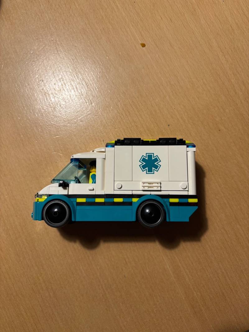 Side profile of a completed LEGO City ambulance model, white and teal with a blue Star of Life emblem