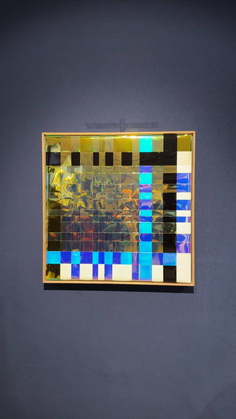 A contemporary wall sculpture with a grid of dichroic tiles that shift from gold to blue, set in a light wood frame. - view 1